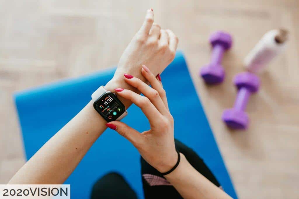 Anonymous sportswoman checking smart watch and sitting on mat