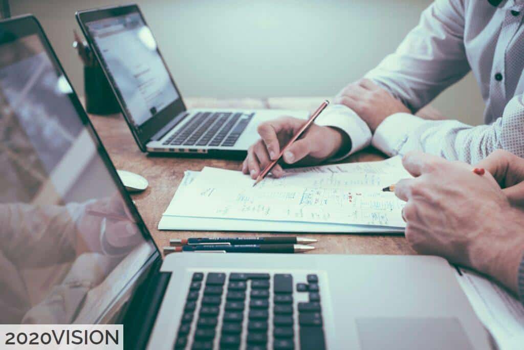 person holding pencil near laptop computer